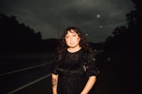 a woman in a black dress standing on a road