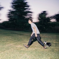 a man walking his dog in a field at dusk